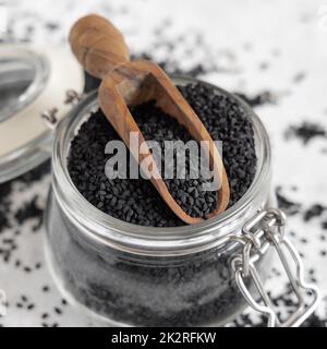 Épices indiennes graines de cumin noir (nigella sativa ou kalonji) dans un pot en verre avec une pelle en bois de gros plan Banque D'Images