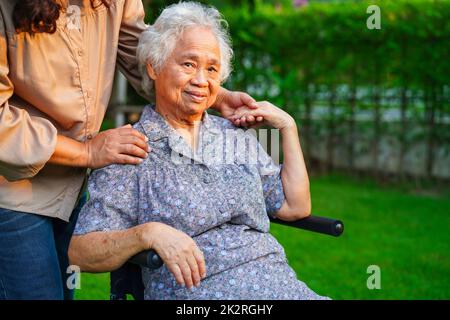 Caregiver help Asian elderly woman disability patient sitting on wheelchair in park, medical concept. Stock Photo