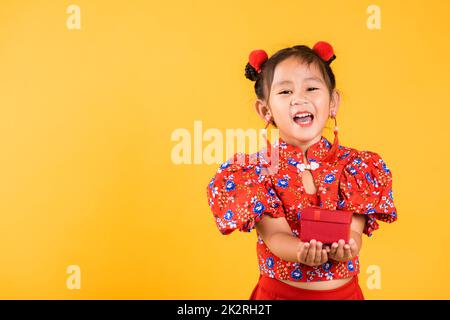 Joyeux petit sourire asiatique chinois port cheongsam rouge tenant boîte cadeau Banque D'Images