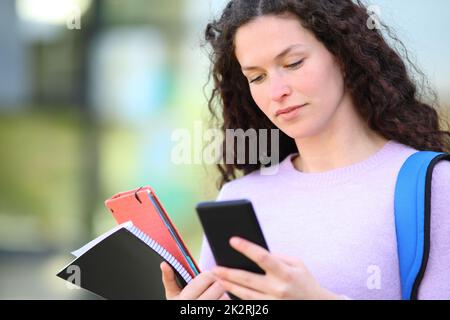 Étudiant sérieux lisant du contenu téléphonique dans un campus Banque D'Images