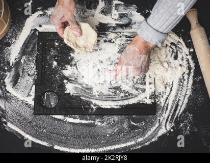 deux mains de femmes pétrient la pâte de farine de blé blanc sur une table noire, vue de dessus Banque D'Images