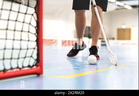 Joueur de ballon de sol. Hockey sur pieds et jeu de bandy intérieur. Boule et bâton blancs. Objectif et filet sur le sol dans l'arène d'entraînement. Jeune homme ou garçon jouant. Banque D'Images