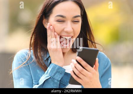 Une femme choquée consulte son smartphone à l'extérieur Banque D'Images