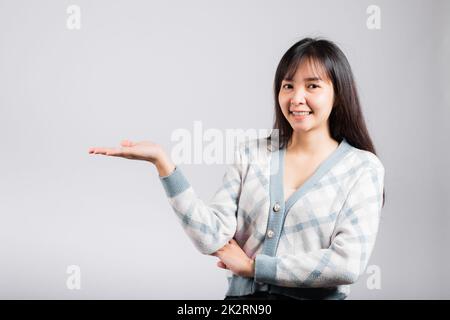 Souriante bonne femme présentant un produit tenant quelque chose sur le côté de la paume Banque D'Images