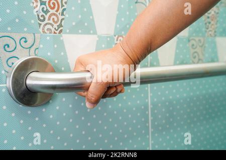 Asian woman patient use toilet support rail in bathroom, handrail safety grab bar, security in nursing hospital. Stock Photo