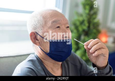 Homme asiatique senior effectuant un auto-test pour COVID-19 à la maison avec Antigen kit. Banque D'Images