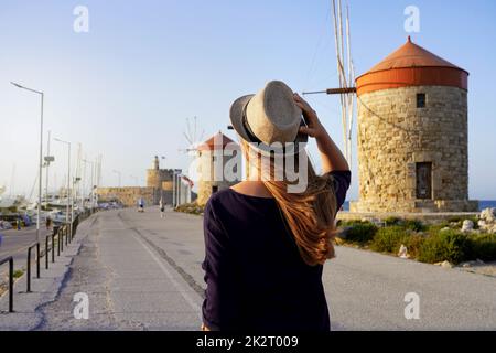 Visite de Rhodes en Grèce. Vue arrière de la jeune femme voyageur marchant le long de la promenade avec les anciens moulins à vent de Rhodes, en Europe. Coucher de soleil. Banque D'Images