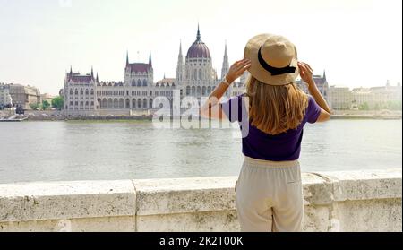 Tourisme en Europe. Vue arrière d'une jeune femme avec chapeau bénéficiant d'une vue sur le Parlement hongrois sur le Danube à Budapest, Hongrie. Banque D'Images