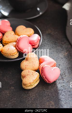 Macarons doux en forme de cœur sur une table noire. Banque D'Images