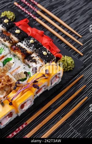 Différents types de sushis servis sur une assiette en pierre dans un restaurant. Magnifique décor et service avec baguettes Banque D'Images