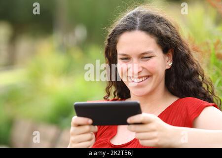 Une femme heureuse dans un parc regardant des vidéos sur un smartphone Banque D'Images