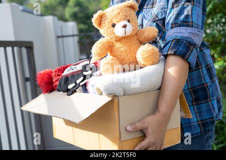 Tenir la boîte de dons de vêtements avec des vêtements usagés et une poupée à la maison pour aider les pauvres dans le monde. Banque D'Images