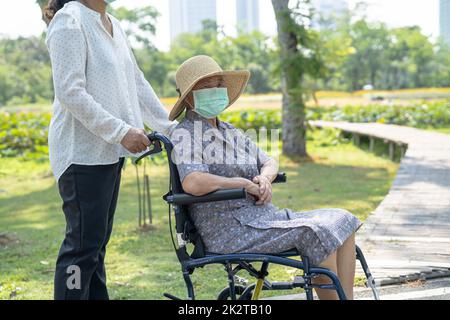 Aidez une femme asiatique âgée ou âgée en fauteuil roulant et portant un masque facial pour protéger l'infection à Covid-19 coronavirus dans le parc. Banque D'Images