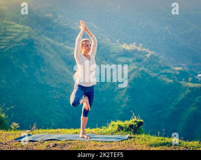 Woman doing yoga asana Vrikshasana posture de l'arbre dans les montagnes à l'extérieur Banque D'Images