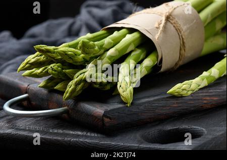 Bouquet d'asperges fraîches crues sur une planche de cuisine noire en bois Banque D'Images