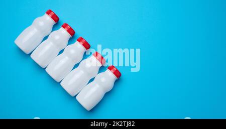 Flacons en plastique blanc avec bouchons rouges pour produits laitiers sur fond bleu, vue de dessus Banque D'Images