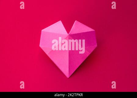 Coeur de papier rose origami isolé sur fond rouge Banque D'Images