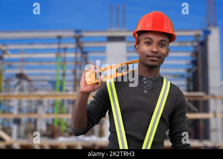 ouvrier de chantier tenant un outil de niveau et portant un casque de sécurité rouge Banque D'Images