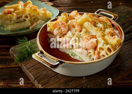 Délicieux plat avec des pâtes et des crevettes dans une casserole et une assiette servie sur une table Banque D'Images