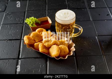 Verre de bière placé près de l'assiette avec des nuggets de poulet sur une table noire Banque D'Images