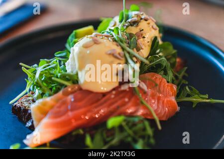 Accent sélectif sur le petit déjeuner sur l'assiette. Œufs benedict avec saumon, arugula avec graines de tournesol. Banque D'Images