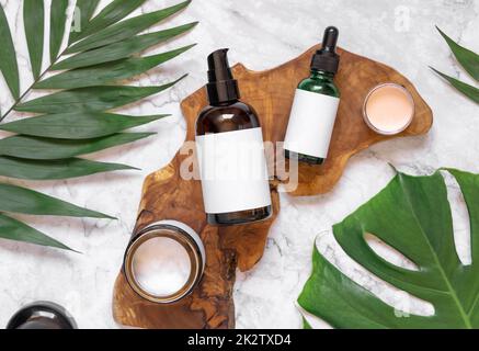 Cosmétiques naturels en bouteilles de verre sur un panneau en bois près des feuilles tropicales, maquette, vue de dessus Banque D'Images