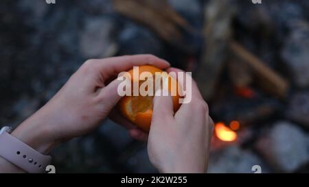 Femme peeling à la main mandarine douce mûre, gros plan au-dessus de la cheminée dans la forêt au camping. Banque D'Images