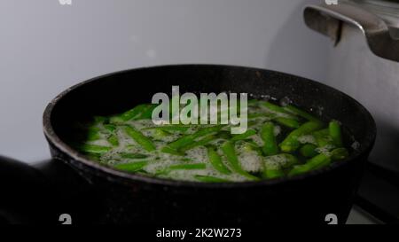 Gros plan sur l'ébullition des haricots verts dans une casserole avec de l'eau bouillante et de la vapeur Banque D'Images