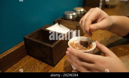 Une femme tenant un café avec de la crème et un bâton de bois et remuant le café chaud sur une table en bois Banque D'Images