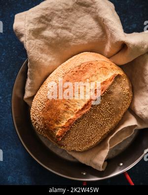 Pain de levain maison fraîchement cuit avec graines de sésame dans un plateau sur fond bleu foncé. Vue de dessus. Banque D'Images