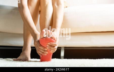 Femme asiatique assise sur un canapé sentant la douleur dans son pied à la maison Banque D'Images