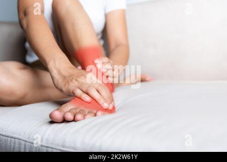 Une femme asiatique assise sur un canapé tient sa cheville blessant la douleur dans son pied à la maison Banque D'Images