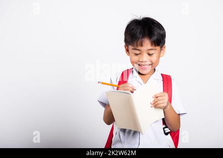 Asiatique tout-petit sourire Happy Wear étudiant thaïlandais uniforme pantalon rouge tenant un crayon pour les écrivains cahier Banque D'Images