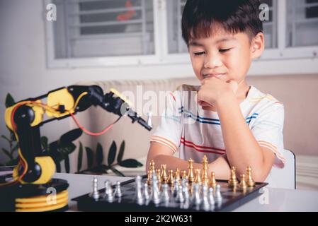 Petit garçon asiatique pensant et attendez bras robot jouant aux échecs Banque D'Images