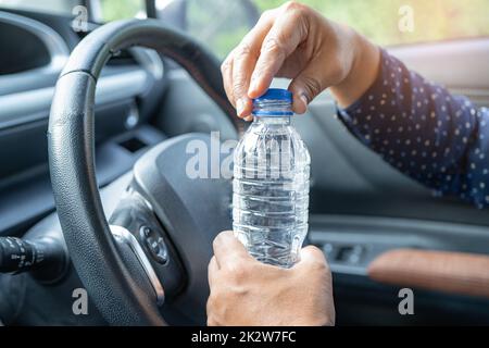 Femme asiatique chauffeur tenant une bouteille pour boire de l'eau tout en conduisant une voiture.Une bouteille d'eau chaude en plastique peut provoquer un incendie. Banque D'Images