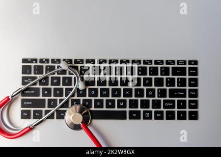 Stéthoscope rouge sur le clavier noir de l'ordinateur sur le bureau blanc montre le bureau numérique des médecins avec des dossiers numériques des patients pour le diagnostic médical et la mesure de cardiologie avec l'antivirus de contrôle hacker attaque Banque D'Images