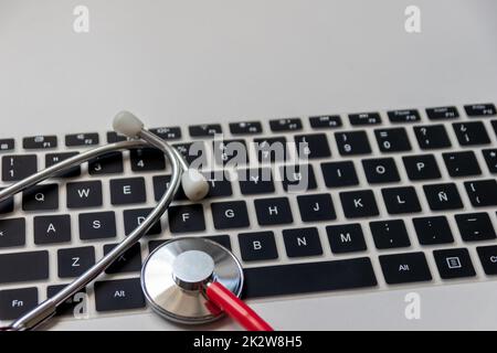 Stéthoscope rouge sur le clavier noir de l'ordinateur sur le bureau blanc montre le bureau numérique des médecins avec des dossiers numériques des patients pour le diagnostic médical et la mesure de cardiologie avec l'antivirus de contrôle hacker attaque Banque D'Images