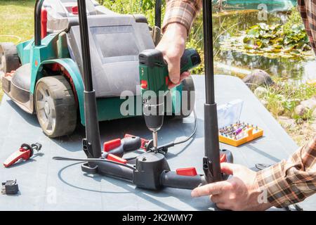 Un homme répare une tondeuse à batterie. L'interrupteur à bascule électrique pour démarrer le moteur est défectueux et doit être remplacé. Un artisan au travail. Banque D'Images