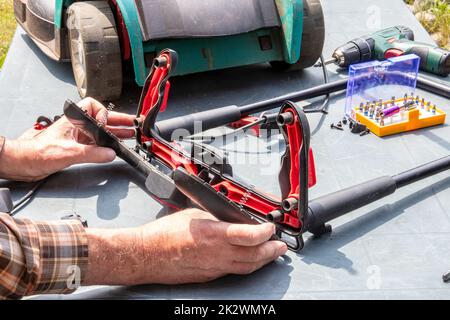 Un homme répare une tondeuse à batterie. L'interrupteur à bascule électrique pour démarrer le moteur est défectueux et doit être remplacé. Un artisan au travail. Banque D'Images