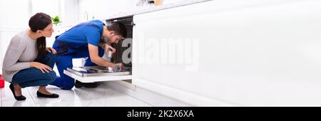 Femme regardant le réparateur de réparation de lave-vaisselle dans la cuisine Banque D'Images