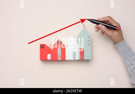 Une maison en bois miniature et une main de femme dessine un graphique avec des indicateurs de croissance. Banque D'Images