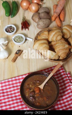 Ragoût de bœuf et pain frais dans une cuisine rustique avec tissus à carreaux rouges et blancs Banque D'Images