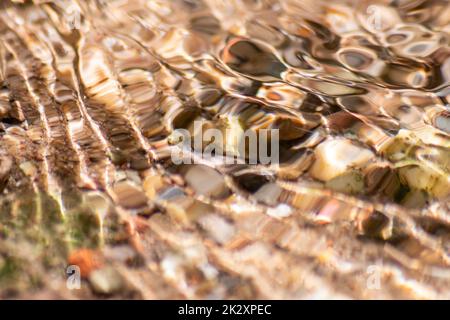 Pierres dans l'eau étincelante avec reflets ensoleillés dans l'eau d'une crique d'eau claire comme le fond naturel idyllique montre la méditation zen, de petites vagues et des ondulations soyeuses dans une source de montagne saine Banque D'Images