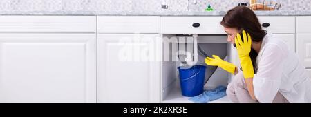 Femme appelant le plombier devant l'eau s'échappant du tuyau Banque D'Images