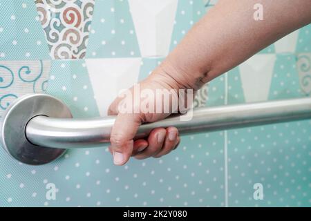 Asian woman patient use toilet support rail in bathroom, handrail safety grab bar, security in nursing hospital. Stock Photo