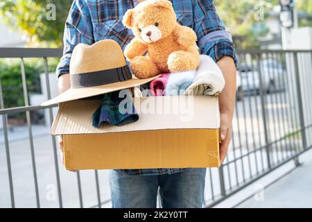 Tenir la boîte de dons de vêtements avec des vêtements usagés et une poupée à la maison pour aider les pauvres dans le monde. Banque D'Images