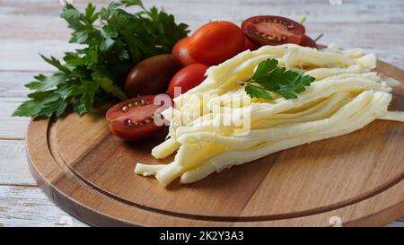 Fromage à cordes ou fouet au fromage - en-cas salé avec tomates cerises et herbes sur la planche à découper. Fromage turc Banque D'Images