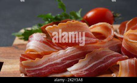 Tranches de bacon fumé aux herbes et aux tomates cerises, tranches de bacon sur planche à découper en bois Banque D'Images