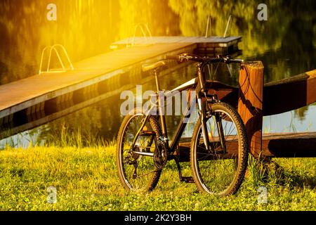 Vélo de montagne sport moderne, adoé à un banc en bois au bord du lac Banque D'Images