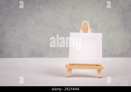 Chevalet avec toile blanche vierge devant un fond texturé gris, cadre pour ajouter des peintures et des images Banque D'Images